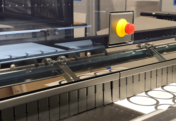 Label sheets moving through an industrial cutting machine with an emergency stop button.